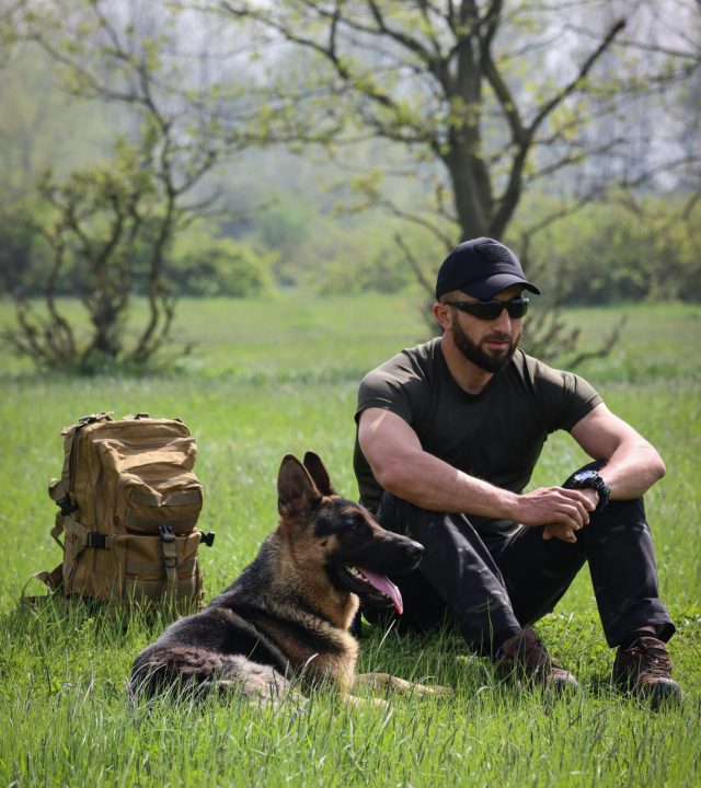 pexels-photo-16148165-16148165 A man and German Shepherd resting in a lush green field under a spring sky in Baku, Azerbaijan.